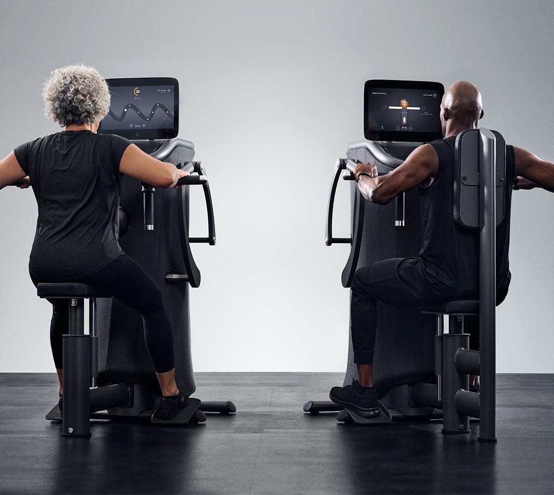Zwei Personen trainieren an EGYM-Kraftgeräten mit Bildschirm